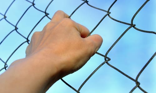 A closeup shot of a female refugee's hand grasping a mesh fence.