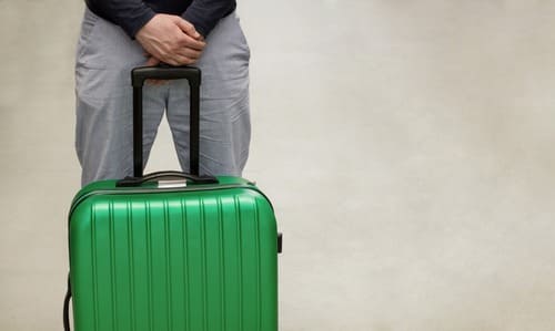 A lower-body shot of a man at an airport with his briefcase, waiting to be deported.