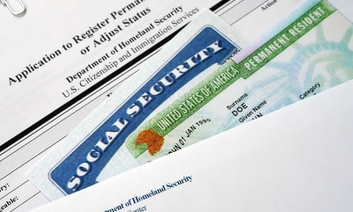 A green card and a social security card stacked on top of an application for permanent residence.