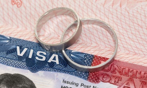 A closeup of two wedding rings stacked and resting on a United States visa.