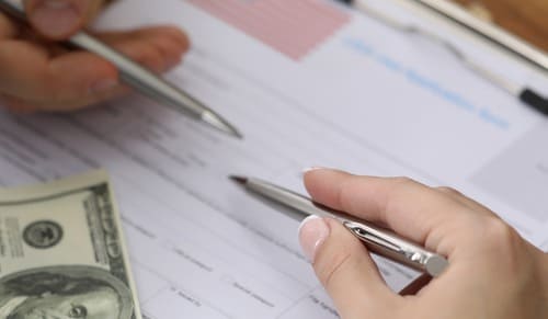 A lawyer's and client's hands filling up a form, with a hundred dollar bill in the foreground.