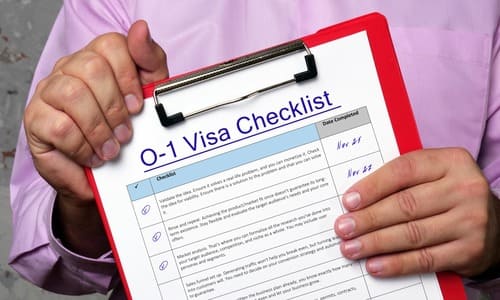 A chest-level image of a man holding up a clipboard with a checklist of requirements for the O1 visa.