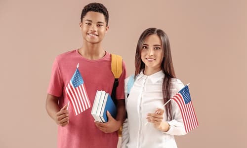 A black male student and white female student wearing backpacks and holding up American flags.
