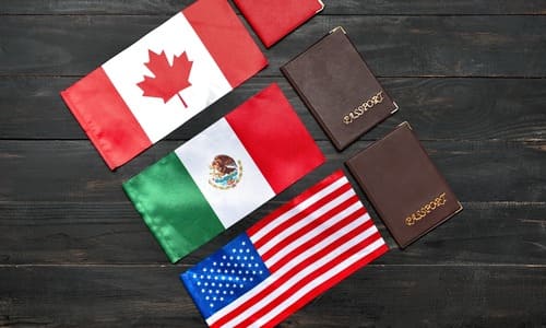 The Canadian, Mexican, and American flags laid out on a darkwood table next to their passports.