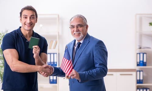 A man holding up his visa and shaking hands with a lawyer who is holding up an American flag.