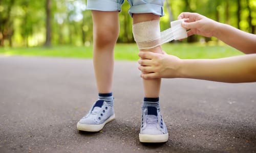 Adult's hands applying bandages to a child's legs after an accident on the playground.