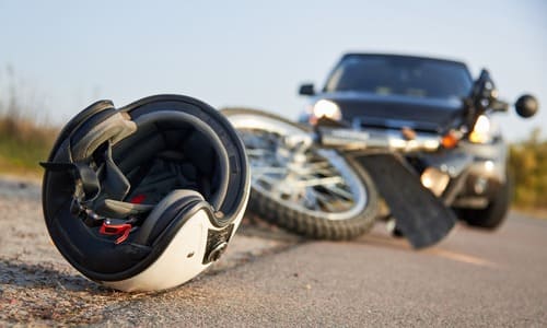 A motorcycle helmet on the road, with a car and motorcycle in the background in the aftermath of a collision.