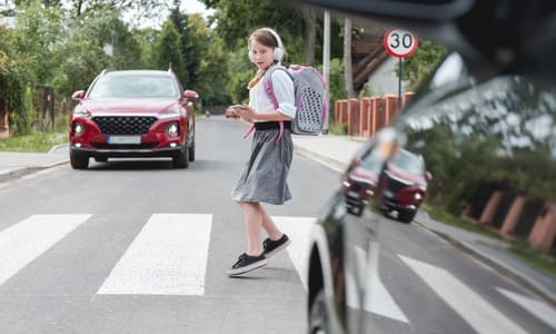 A girl crossing the road with headphones turning to face an oncoming car.