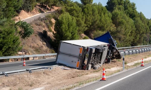 An overturned truck in between two lanes of a highway after an accident.