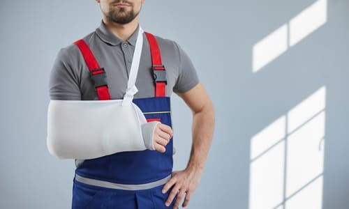 An injured worker with his right arm in a cast and sling, and his left arm on his hip.