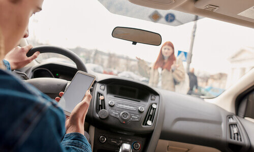 Distracted driver looking at his phone about to run over a female pedestrian.