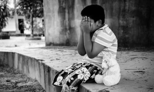 A black and white photo of an Indian child crying and covering his face.
