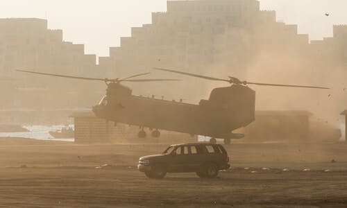 An American CH-47 Chinook helicopter llifting off and a vehicle next to it emptied of passengers.