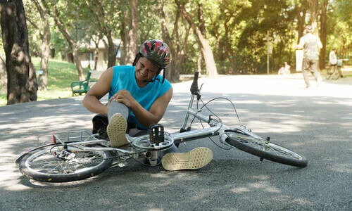 Cyclist injured and grasping his knee in pain after falling off his bicycle.