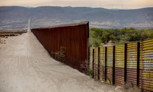 A section of fence between the USA and Mexico along a highway, stretching into the distance.