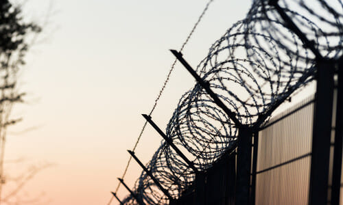 The silhouette of a barbed wire fence against the sky at sunset.
