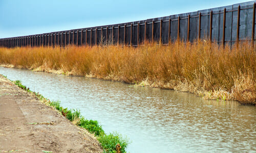 The border fence between Mexico and the US, with a small river flowing next to it.