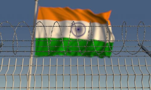 The Indian flag blowing in the wind behind a barbed wire fence.