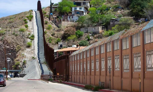 A section of fence along the US-Mexico border separating a Mexican town from an American road.