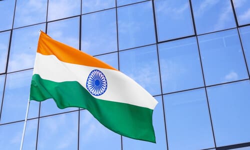 The Indian flag waving in front of a building with large reflective windows.