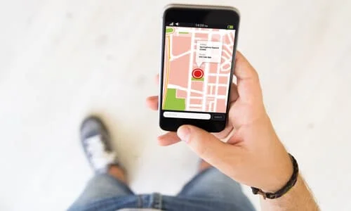 A first-person shot of a man looking down on his phone and booking a rideshare on his phone.