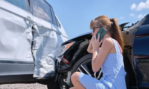 A woman calling a lawyer on her phone after an accident with another vehicle.