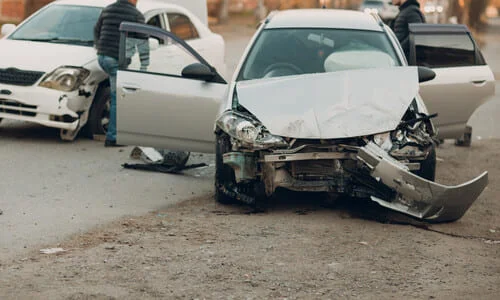 A totaled silver-grey car in the middle of a city street after a vehicular accident.