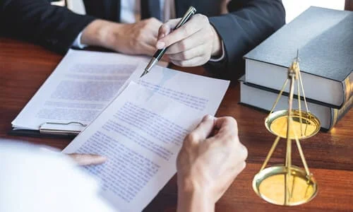 A lawyer behind their desk pointing at lines on a clipboard while explaining them to a client.