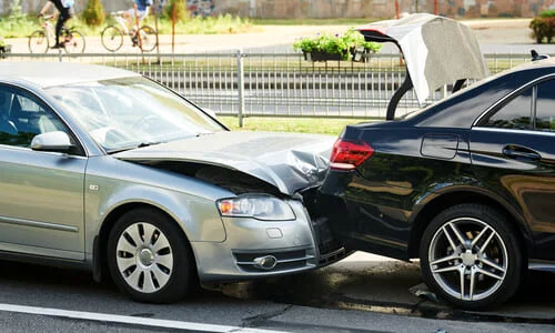 A rear-end accident between a silver and a black car on a suburban road.