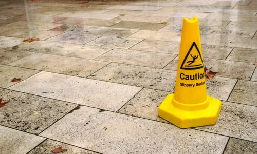 A wet floor with a yellow safety cone warning of a slippery surface.