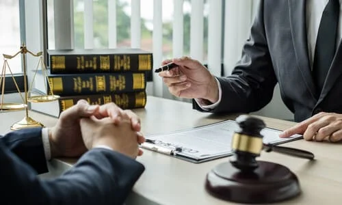 A low-angle image of a lawyer discussing documents with a client from behind a desk.