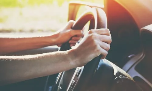 A near shot of a driver's hands firmly grasping a steering wheel in the afternoon.