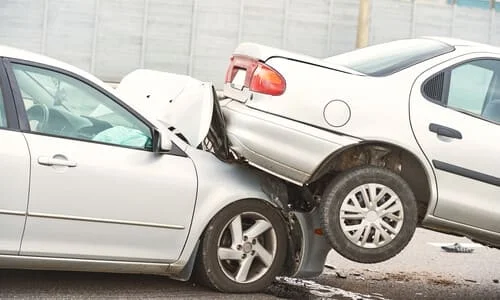 Two white cars in a serious rear-end accident with one mounted on top of the other's hood.