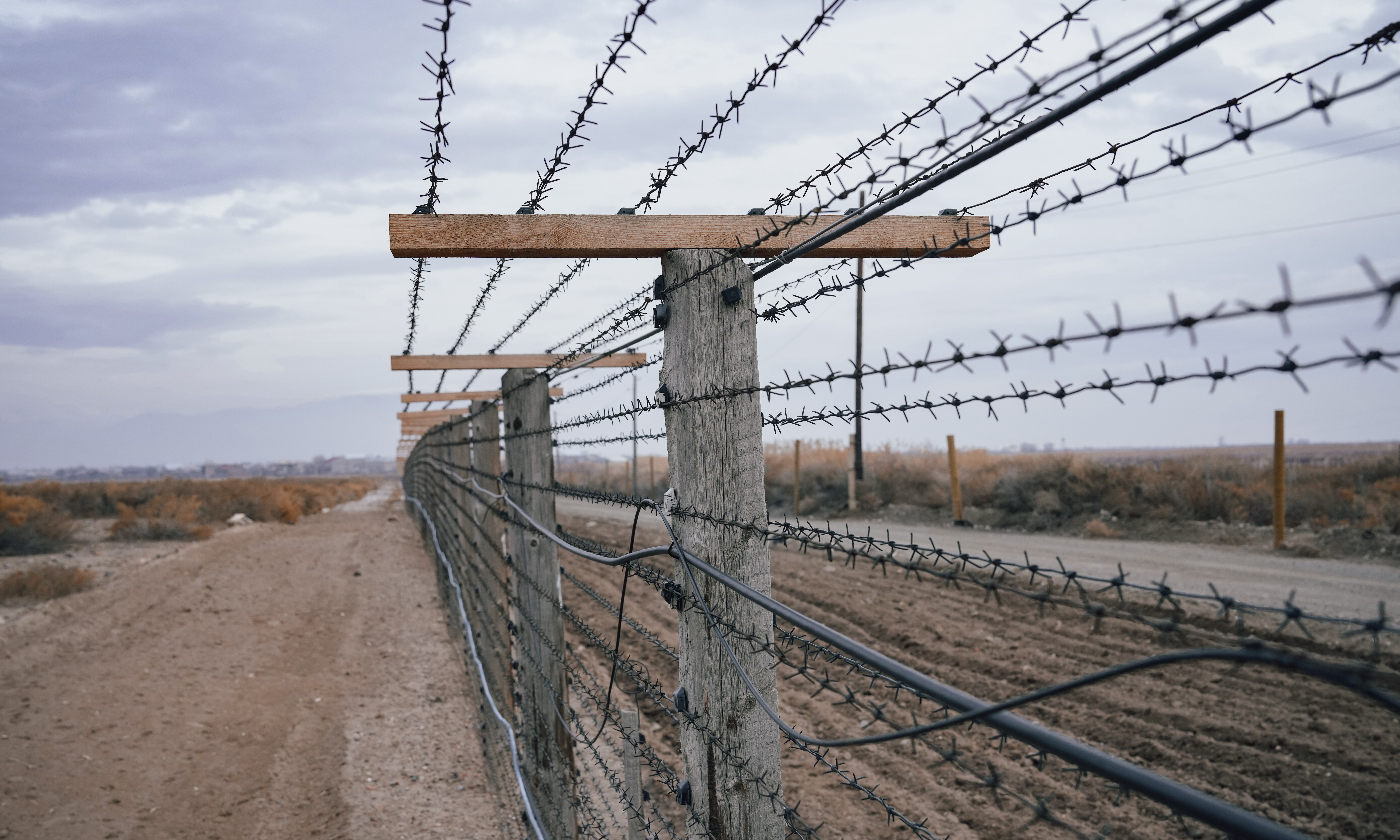 A barbed wire fence next to a road at the border of the United States.
