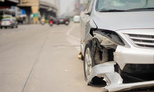 A front shot of a damaged front bumper of a grey car involved in an accident.