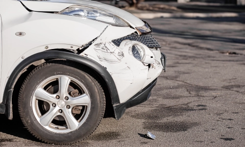 A near profile shot of a white car's crumpled front end after an accident.