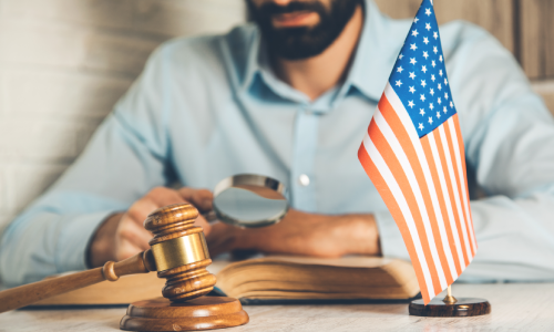An E2 visa lawyer reading fine print on documents with a magnifying glass while seated at a desk.