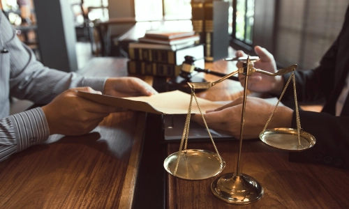 A client handing documents to an Avenal personal injury lawyer at a table with legal books and scales of justice.