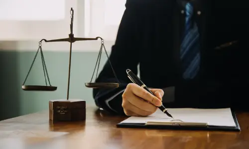 A Copperopolis personal injury lawyer writing notes at his desk with a scale of justice placed beside him.