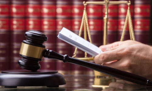 A close-up photo of a gavel hammer with the scale of justice in the background and the hand of a Cutler personal injury lawyer holding legal documents.