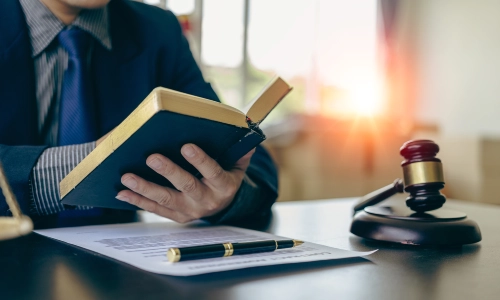 A Dinuba personal injury lawyer reading a book at a desk with a paper, pen, and gavel hammer placed on it.