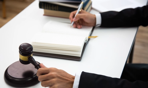 An Empire personal injury lawyer taking notes while holding a gavel hammer, with law books visible in the background.