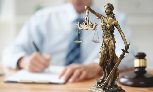 A Lathrop Personal Injury Lawyer writing on a clipboard behind a close up of a Lady Justice figure.