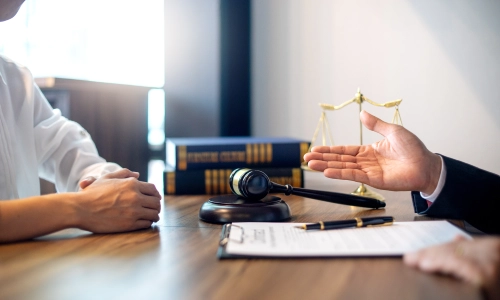 A Livingston personal injury lawyer giving legal advice to his client during a meeting, with documents, a pen, a scale of justice, law books, and a gavel hammer placed on the table.