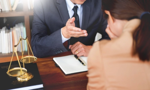 A Manteca personal injury lawyer explaining the legal intricacies of a case to an overwhelmed and frustrated client during a meeting, with a notebook, pen, books, and a scale of justice on the table.