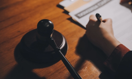 A Merced personal injury lawyer writing notes with his left hand, with a gavel hammer visible in the foreground.