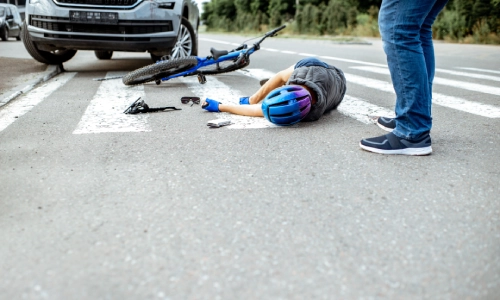 An injured cyclist lying on a pedestrian crossing near his broken bicycle, in need of a San Antonio bicycle accident lawyer.