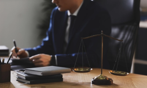 A Daycare Accident Lawyer in a San Antonio law office signing a document while sitting at a table with scales of justice on top.