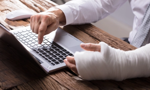 A man wearing a bandage on his injured arm is consulting a Riverbank personal injury lawyer through his laptop regarding the accident that caused his injury.