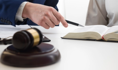 A Shafter Personal Injury Lawyer discussing a case with a client while holding a pen in their hand and pointing to a book on an office table.